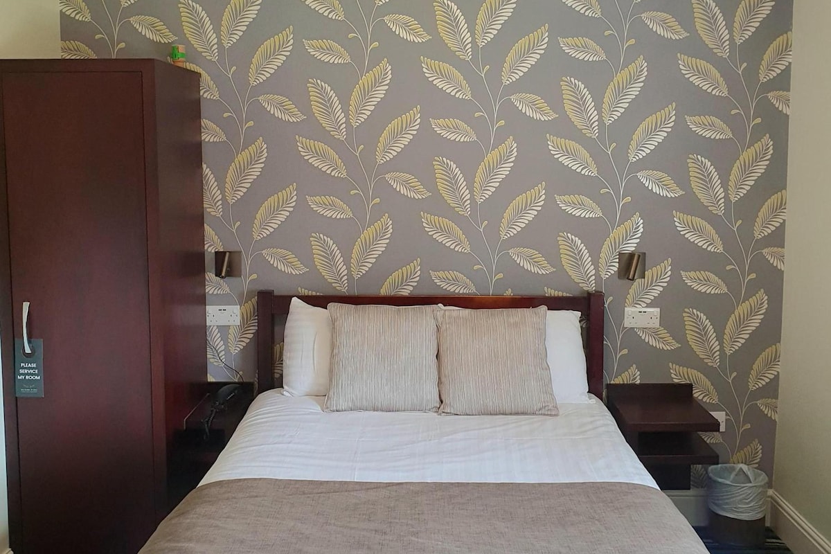 A hotel room with a bed, a wooden wardrobe, and a wall with a leaf pattern.