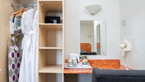 A hotel room with a wooden wardrobe, a mirror, a small table with toiletries, and a chair. - The Lanes Hotel (Brighton)