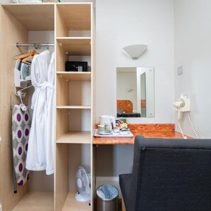 Een hotelkamer met een houten garderobe, een spiegel, een klein tafeltje met toiletartikelen en een stoel.