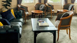 A room with a leather sofa, two armchairs, a coffee table, and a view through large windows with curtains. - The Lanes Hotel (Brighton)