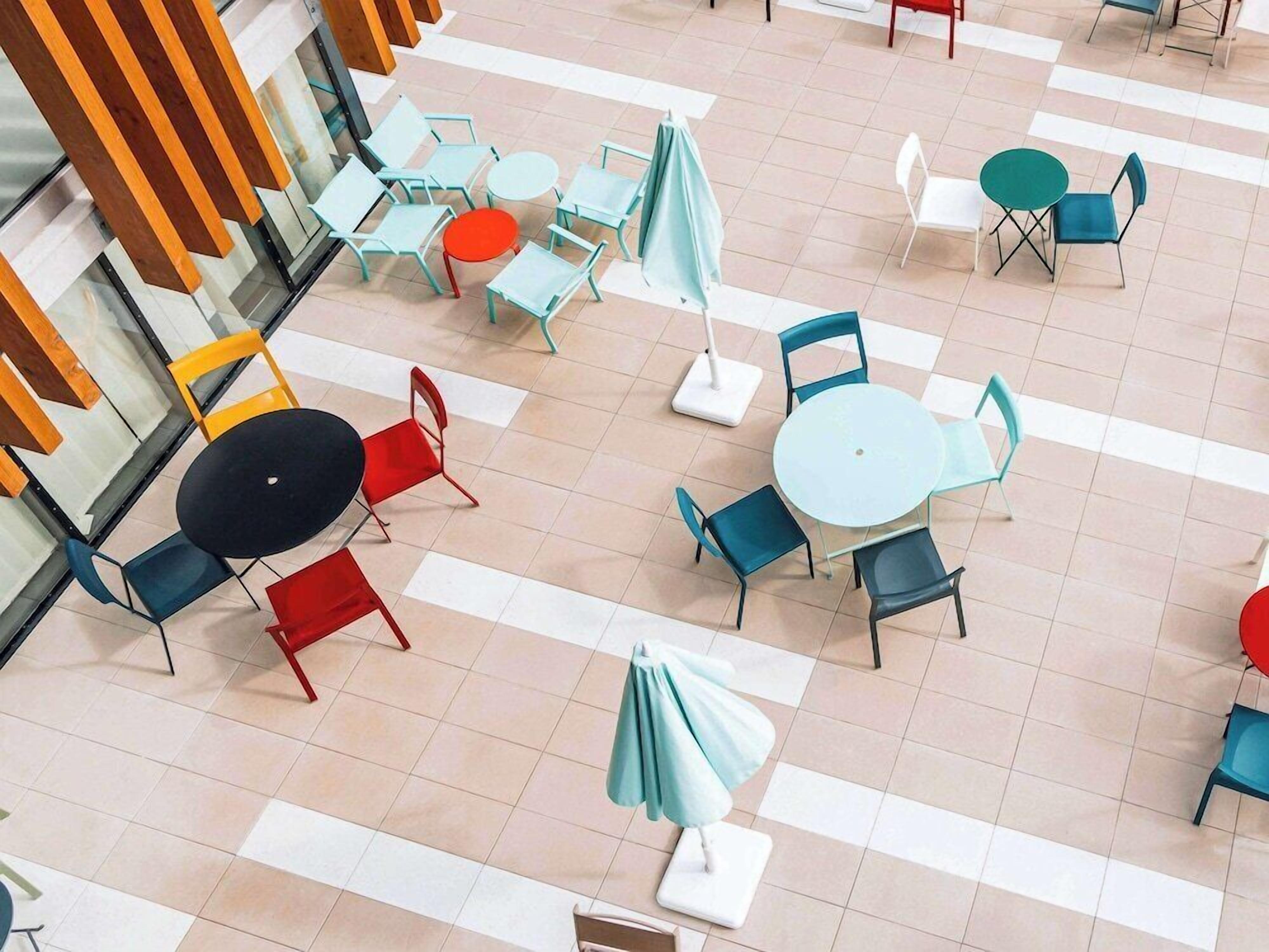 An outdoor café area with multiple tables and chairs, some with umbrellas.