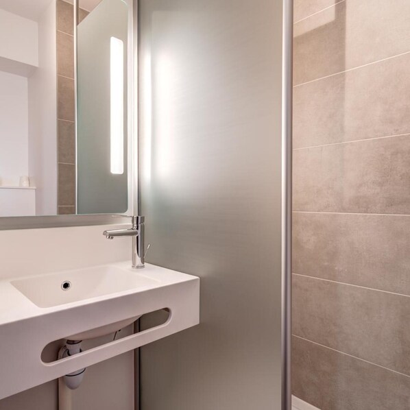 A modern bathroom with a white sink, a mirror, and a shower area. - B&B Hotel Le Port Marly Saint Germain en Laye (La Haute-Maison)