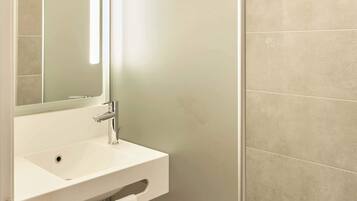 A bathroom with a white sink, a mirror, and a wall with beige tiles.