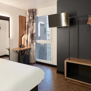 Habitación de hotel con cama, escritorio con lámpara, armario y ventana grande.