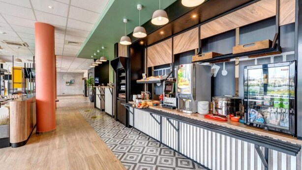 A modern kitchen area with a long counter, various appliances, and a refrigerator. - B&B Hotel Le Port Marly Saint Germain en Laye (La Haute-Maison)