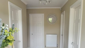 A hallway with wooden flooring, white doors, a radiator, and a wall clock. - The Royal Court Hotel (Portrush)