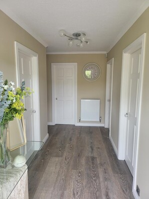 A hallway with wooden flooring, white doors, a radiator, and a wall clock. - The Royal Court Hotel (Portrush)