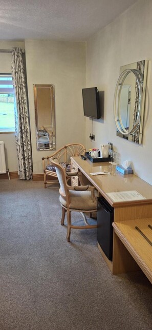 A hotel room with a wooden desk, two chairs, a television, a mirror, and a window with curtains. - The Royal Court Hotel (Portrush)