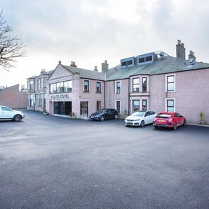A hotel with a name sign, a parking lot with several cars, and a building with a brick facade. - Palace Hotel (Peterhead)