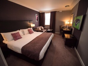 A hotel room with a large bed, a desk, a chair, a TV, and a window with curtains. - Palace Hotel (Peterhead)