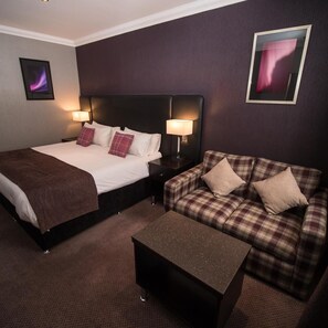 A hotel room with a bed, a sofa, a coffee table, and two nightstands with lamps. - Palace Hotel (Peterhead)