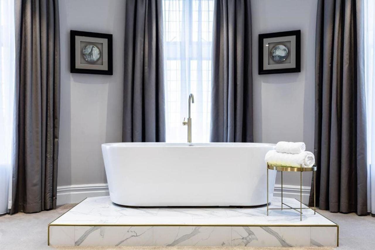 A modern bathroom with a freestanding bathtub, a marble-tiled floor, and a small table with towels.