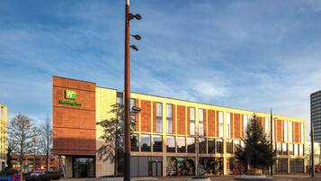 A Holiday Inn hotel with a modern design, featuring a prominent logo, large windows, and a well-maintained outdoor area with trees and a paved walkway.