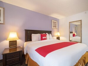 Une chambre d’hôtel avec un lit, deux tables de chevet, un miroir et un tableau accroché au mur.