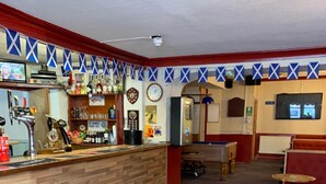A bar area with a wooden counter, multiple stools, and a seating area with tables. - Grant Arms Hotel (Buckie)