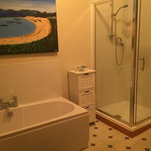 A bathroom with a bathtub, a glass shower enclosure, and a painting of a beach scene on the wall. - Grant Arms Hotel (Buckie)
