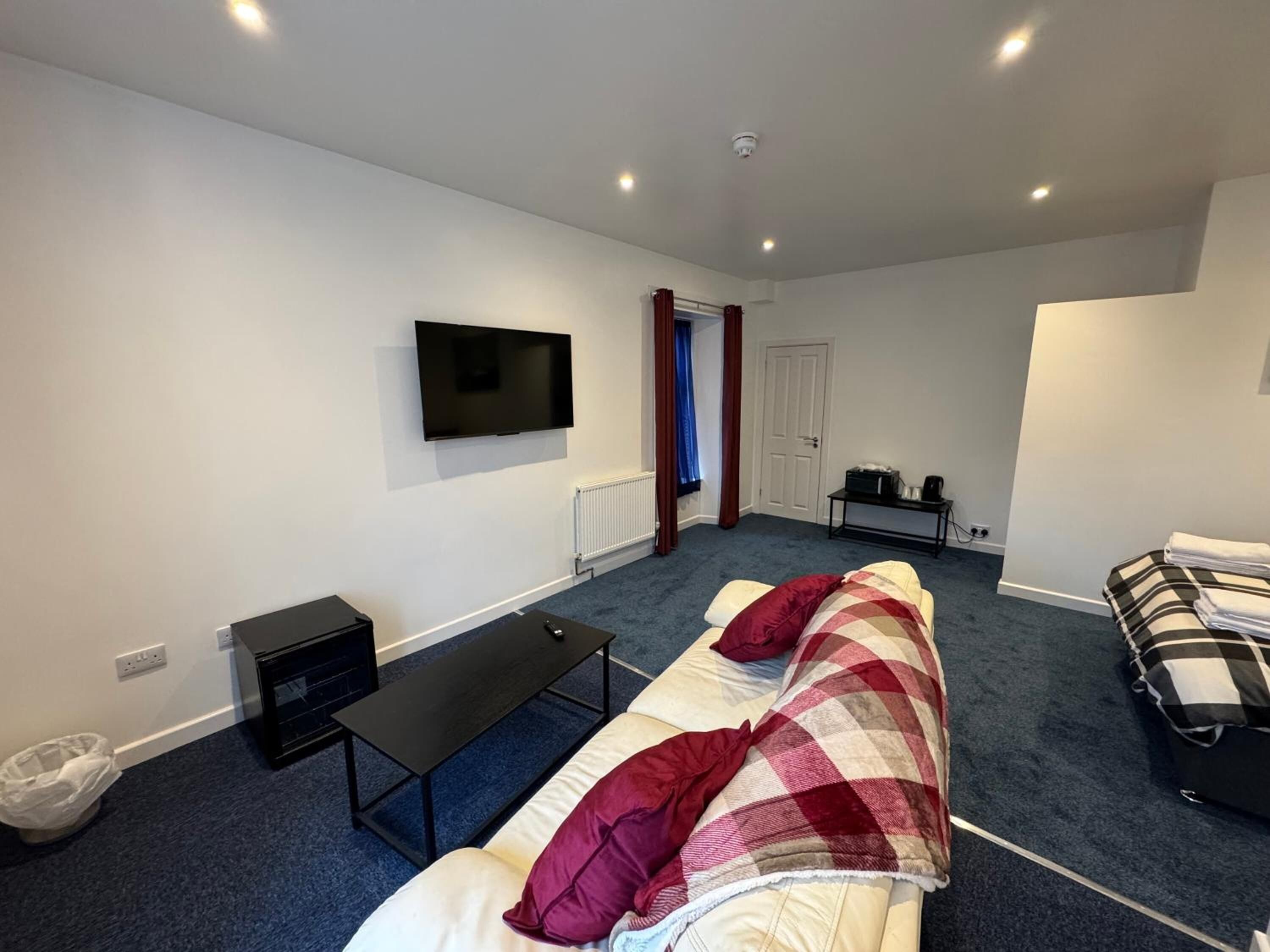 Habitación de hotel compacta con una cama individual, un banco, un televisor montado en la pared y una mesita con una tetera.