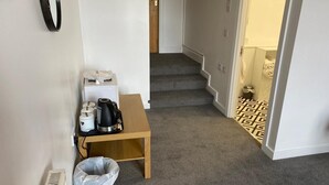A hallway with a small table, a trash bin, and a staircase leading to a bathroom. - Grant Arms Hotel (Buckie)
