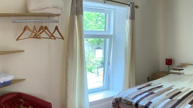 A bedroom with a bed, a red chair, a window with curtains, and a shelf with towels. - Grant Arms Hotel (Buckie)