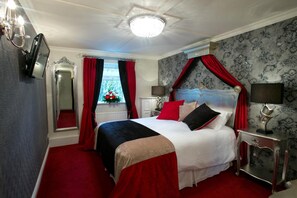A bedroom with a four-poster bed, a mirror, a bedside table with a lamp, and a window with red curtains. - Greenvale Hotel & Restaurant (Cookstown)