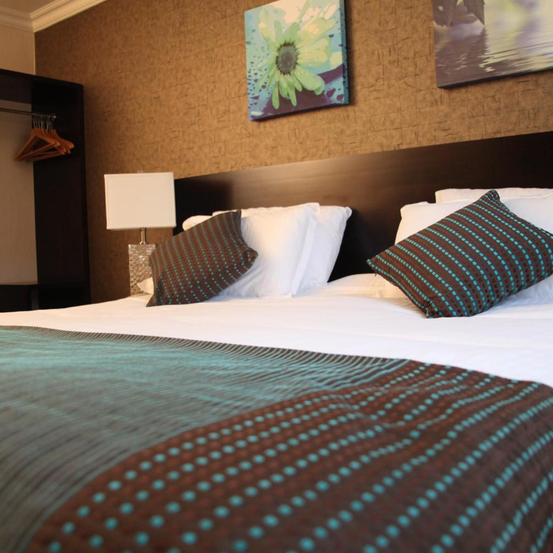 A hotel room with a large bed, a nightstand, a lamp, and a painting on the wall.