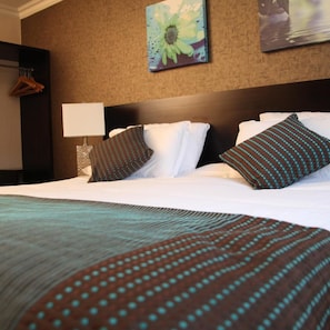 A hotel room with a large bed, a nightstand, a lamp, and a painting on the wall. - Greenvale Hotel (Cookstown)
