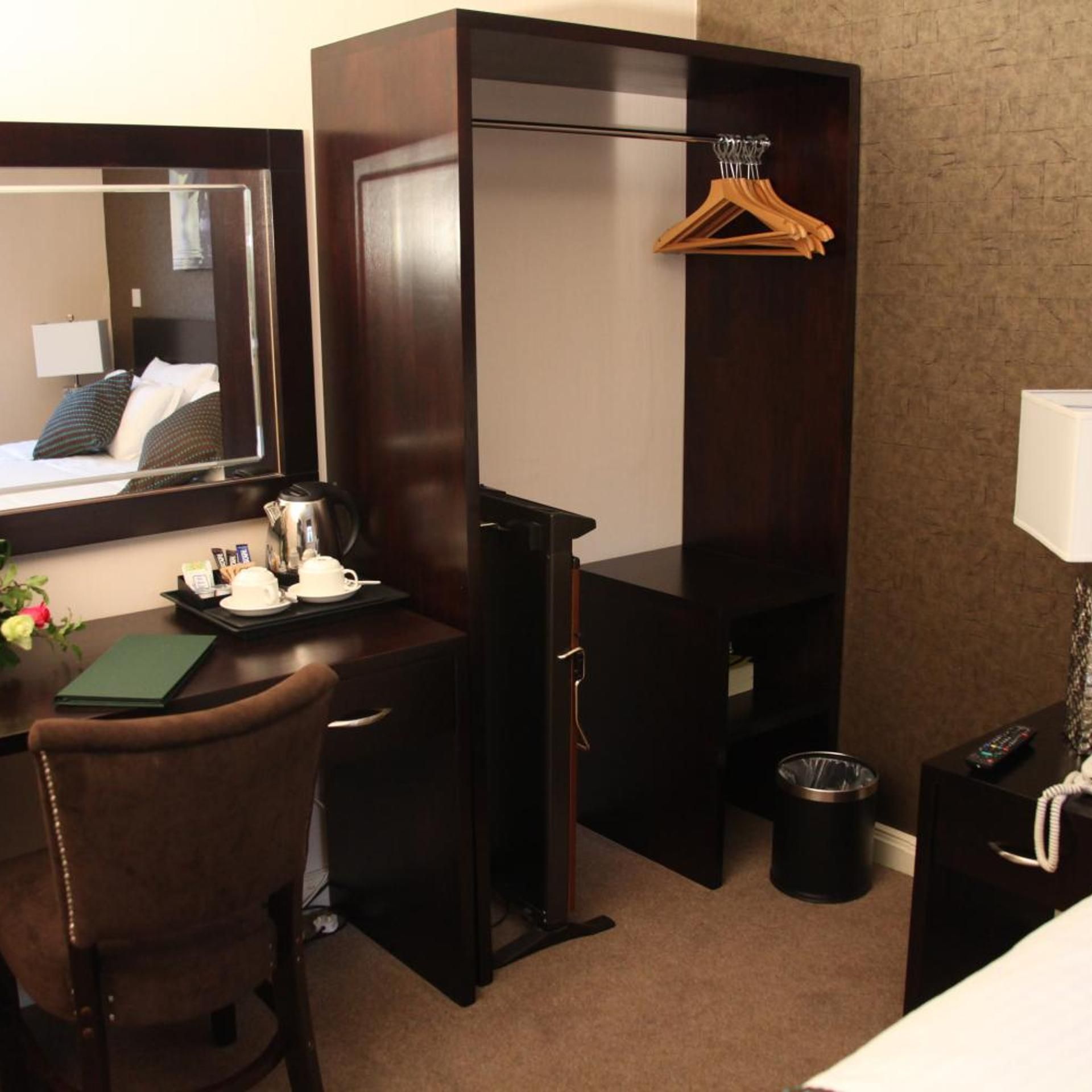 A hotel room with a desk, chair, mirror, and a small table with a tray of tea and a green folder.