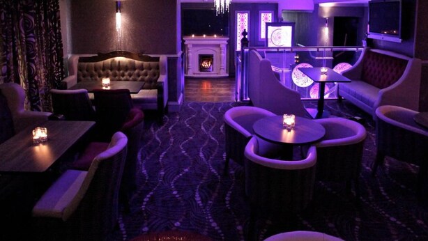 A dimly lit lounge area with plush seating, a fireplace, and a television. - Greenvale Hotel (Cookstown)
