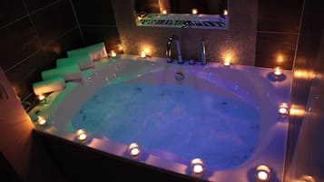 A large bathtub with multiple faucets, surrounded by candles, and a zebra-striped sign above it.