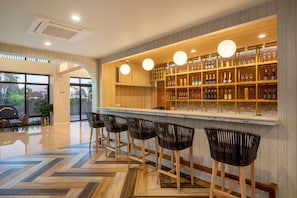 Un espace bar doté d’étagères en bois remplies de bouteilles et de verres, d’un comptoir en marbre et de quatre tabourets de bar noirs en osier.