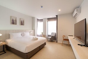 A hotel room with a bed, a desk, a chair, a TV, and two windows with curtains.