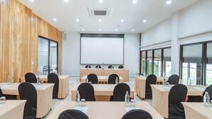 Ein Konferenzraum mit mehreren Tischen und Stühlen, einer Projektionsleinwand und großen Fenstern.