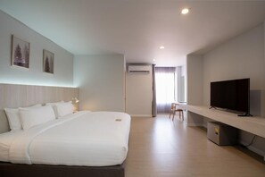 Een hotelkamer met een groot bed, een televisie op een standaard, een airconditioning en een bureau met een stoel.