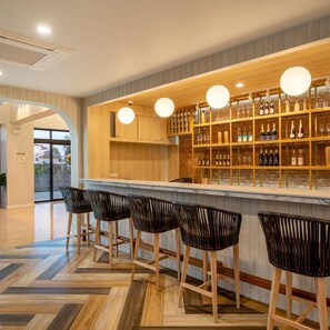 Un espace bar avec des chaises en bois, un comptoir avec des bouteilles et un mur en briques.