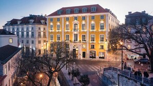 Un edifici de diversos pisos amb una entrada central, envoltat d'altres edificis, en un entorn urbà.