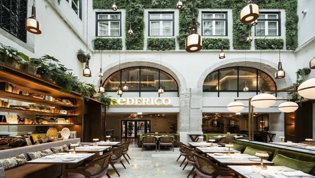 Un restaurant amb una zona de seients central, una barra a l'esquerra i una paret verda amb plantes sobre l'entrada.