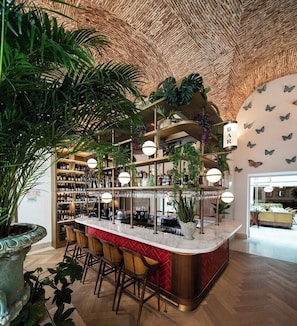 Una zona de bar con una barra curva, varias estanterías llenas de botellas y plantas colgantes.