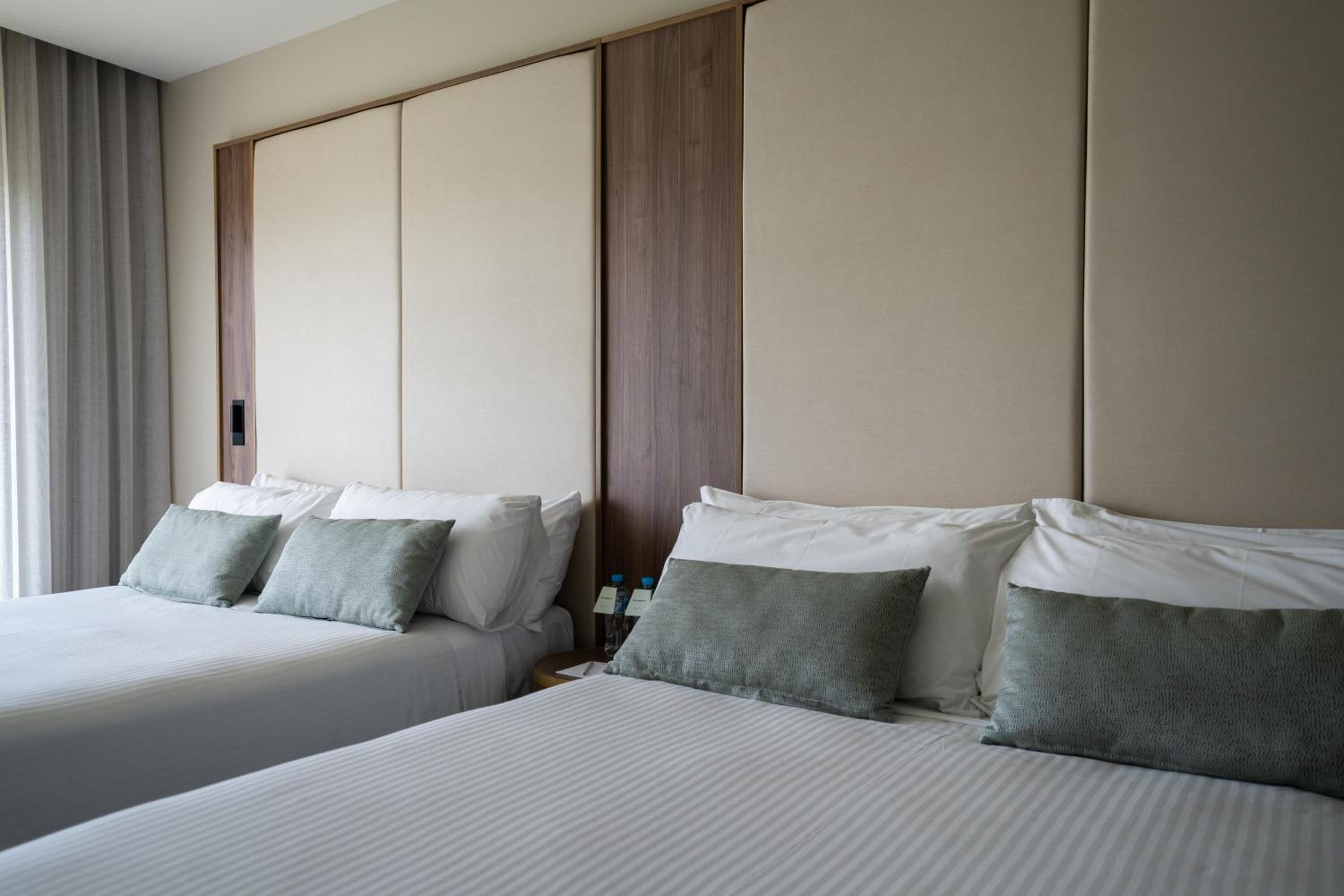 Una habitación de hotel con dos camas, un cabecero de madera y una mesita de noche con una lámpara.