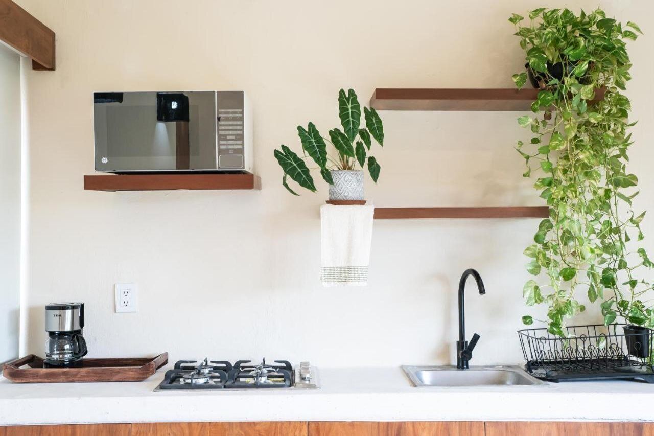 Een keuken met een magnetron, koffiezetapparaat, gasfornuis, spoelbak en twee hangende planten.
