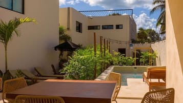 Un patio al aire libre con piscina, mobiliario de mimbre y plantas tropicales.