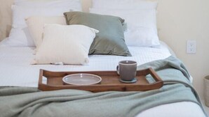 Ein ordentlich bezogenes Bett mit einer grünen Tagesdecke, ein Holztablett mit Tasse und Teller sowie verschiedene gewebte Wandbilder.