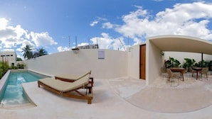 Ein Poolbereich mit Liegestuhl und Tisch, umgeben von einer niedrigen Mauer und einer überdachten Sitzgruppe.