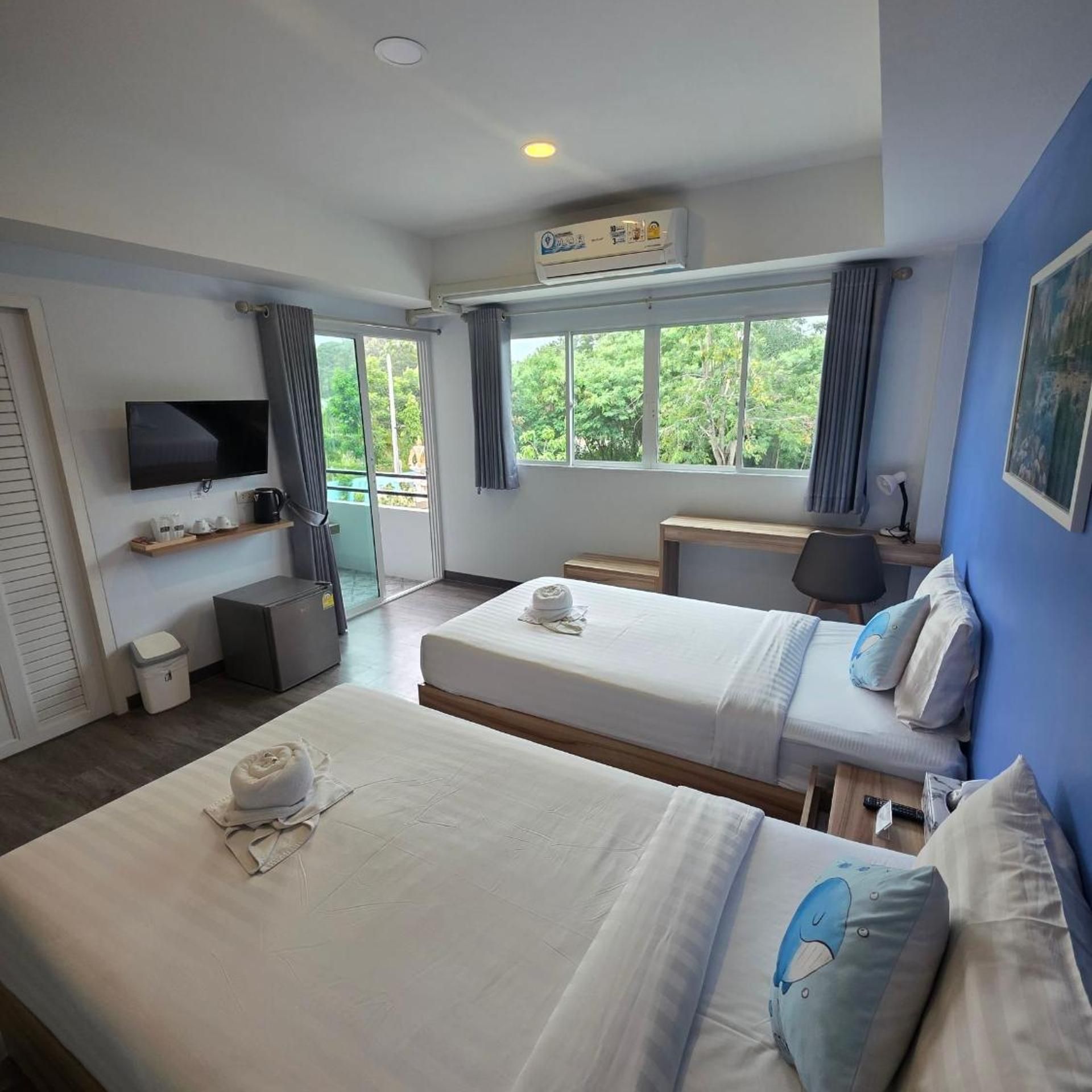 A hotel room with two beds, a desk, a television, and a window with a view of greenery.