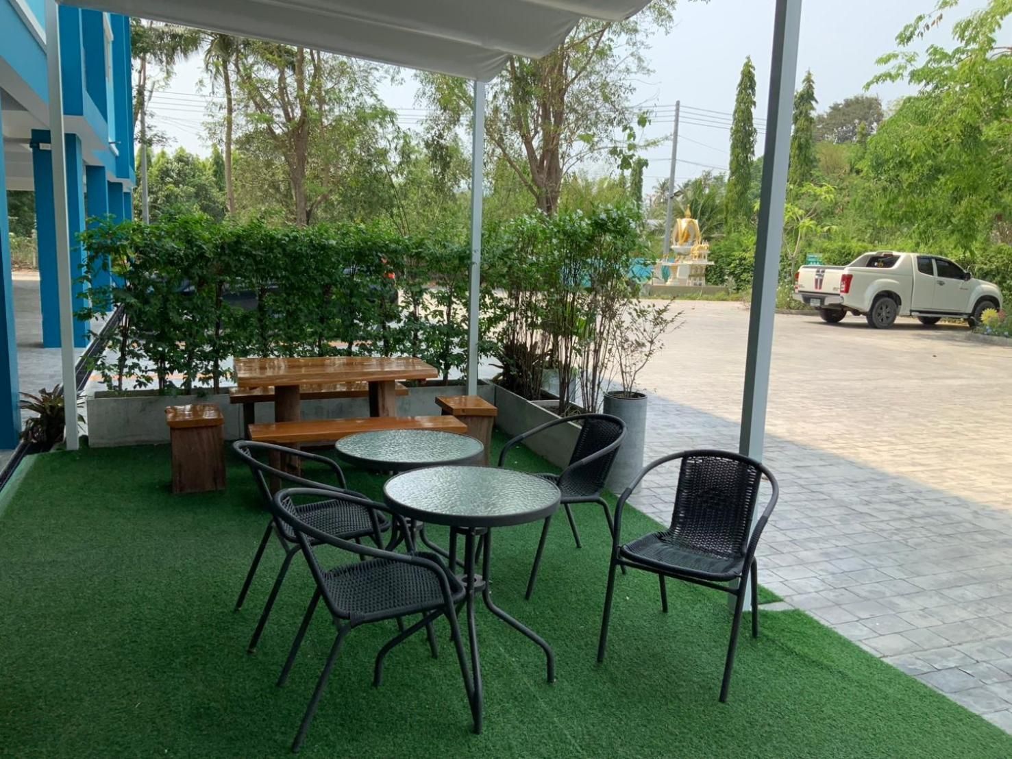 An outdoor patio with tables and chairs, surrounded by greenery and a view of a street.