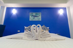 A hotel room with a blue accent wall, a painting of a whale, and a bed with towels arranged in a swan shape. - Bleu Marine Sattahip (Sattahip)