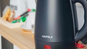 Een zwarte elektrische waterkoker op een houten plank met een televisie erboven.