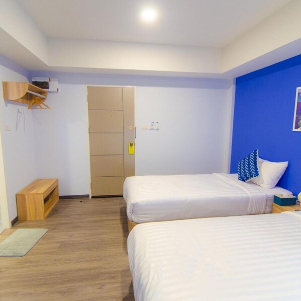 Ein Zimmer mit zwei Betten, einem Kleiderschrank, einer kleinen Holzbank und einer blauen Akzentwand.