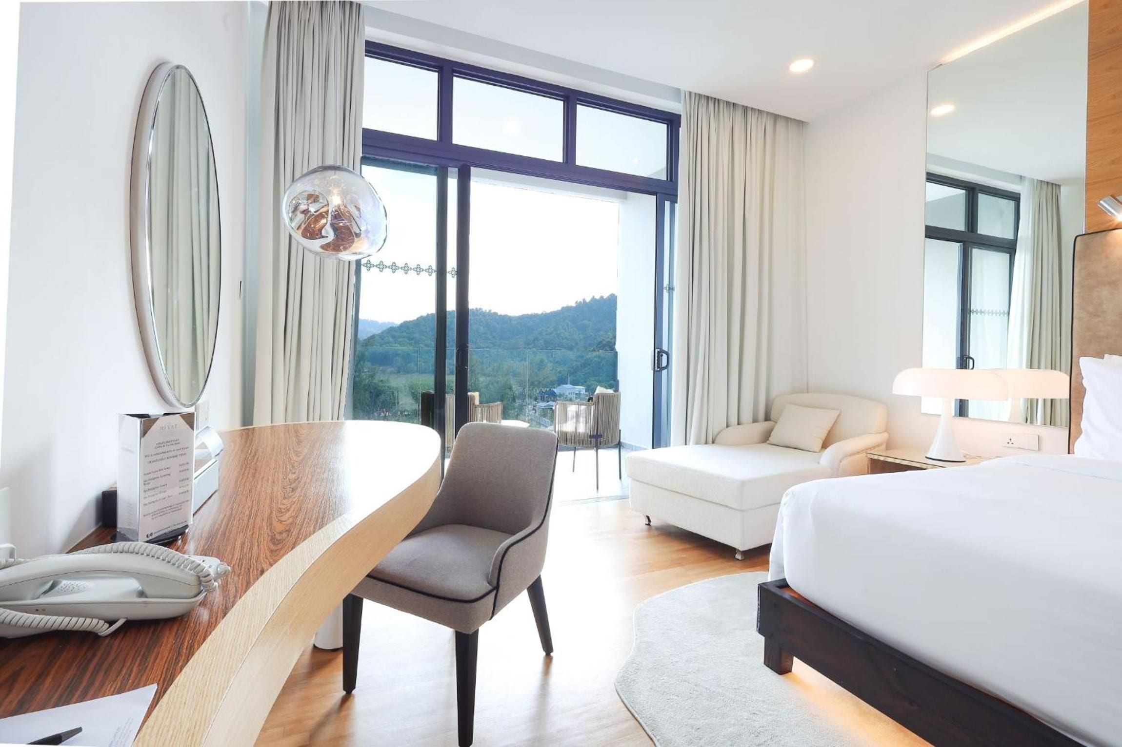 Une chambre d’hôtel équipée d’un lit, d’un bureau, d’une chaise, d’un canapé et d’une grande fenêtre donnant sur l’extérieur.