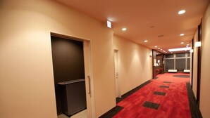 A hotel corridor with a red carpet, doors, and a reception area in the distance. - Ai Hotel Hashimoto (Sagamihara)