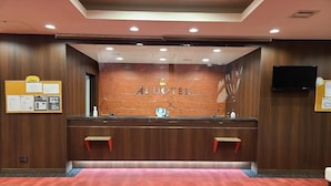 A reception desk with a wooden panel design, a digital screen, and a red carpeted floor. - Ai Hotel Hashimoto (Sagamihara)